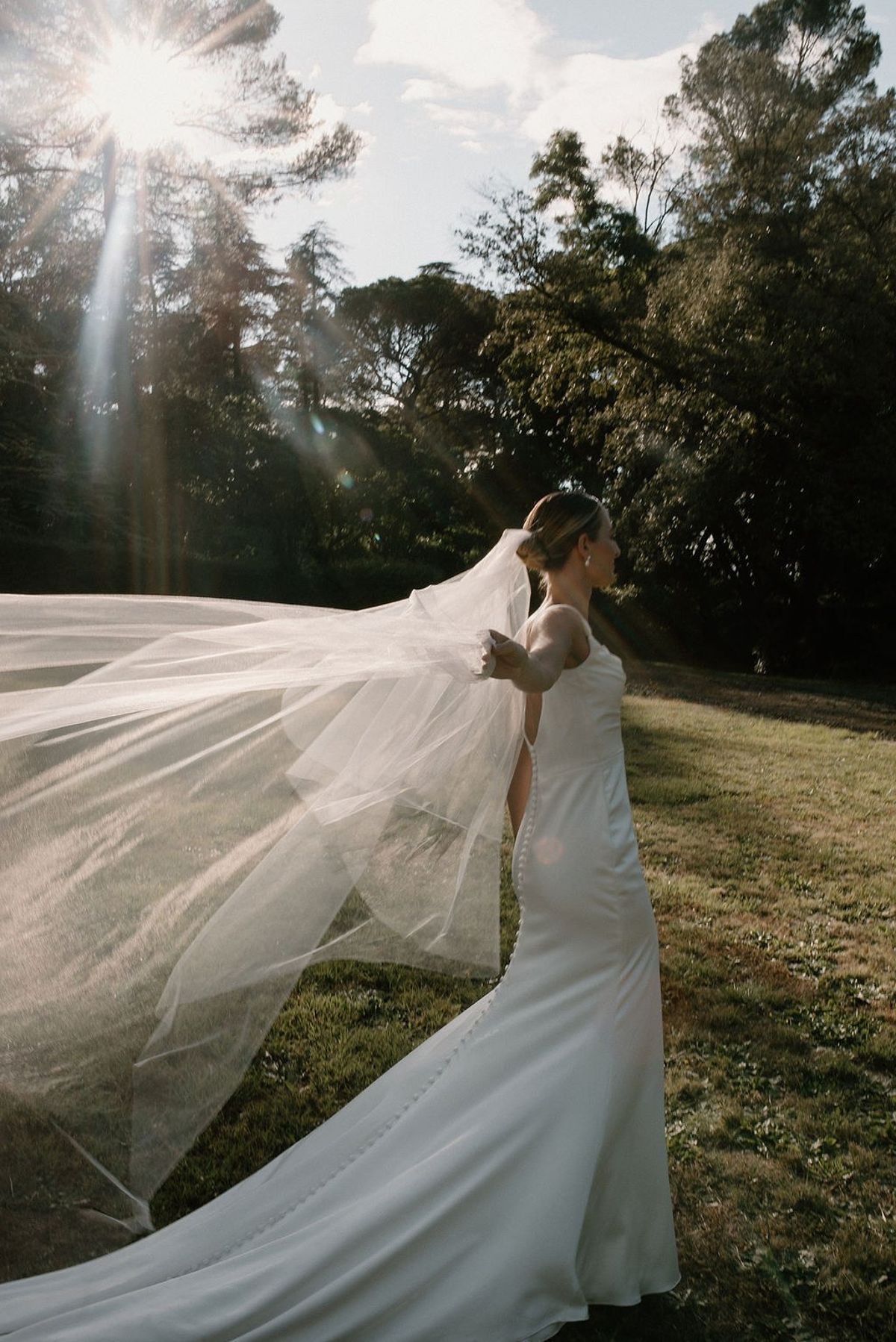 Bride with cathedral veil lifting in late afternoon sun and tree line at Château Sainte-Roseline