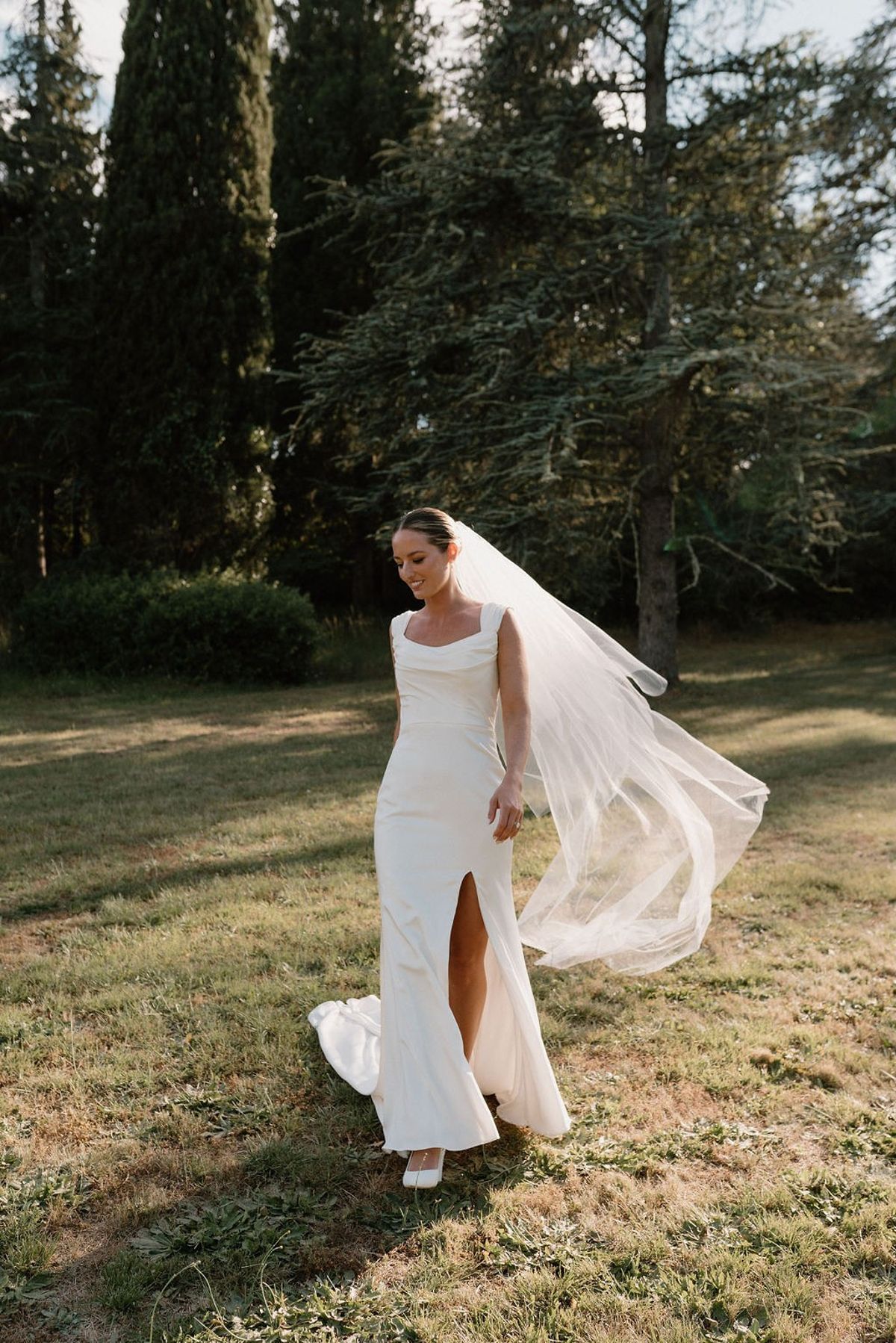 Bride walking through grounds with cypress trees and drifting veil at Château Sainte-Roseline