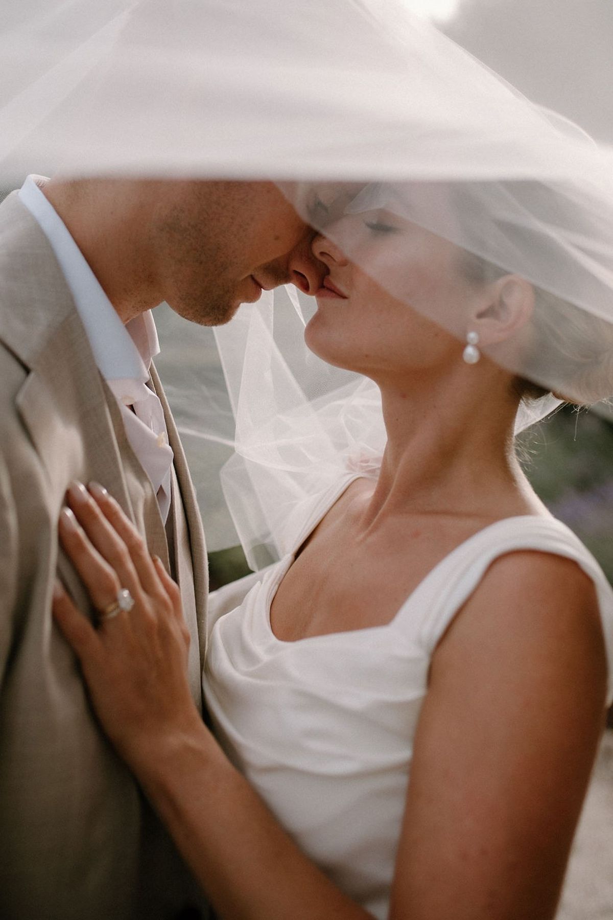 Couple noses touching beneath cathedral veil with pearl drop earring catching the light at Château Sainte-Roseline