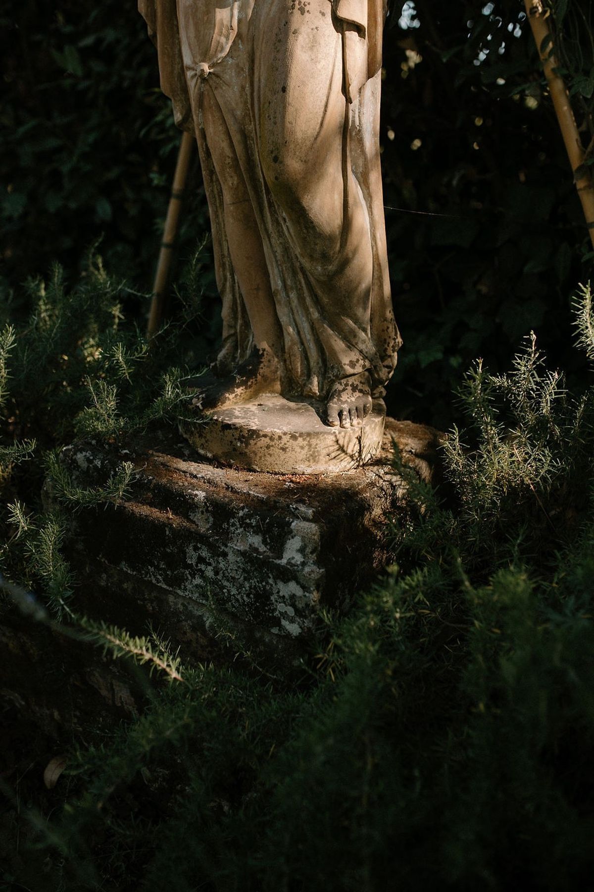 Weathered stone garden statue lit by warm side light among rosemary at Château Sainte-Roseline
