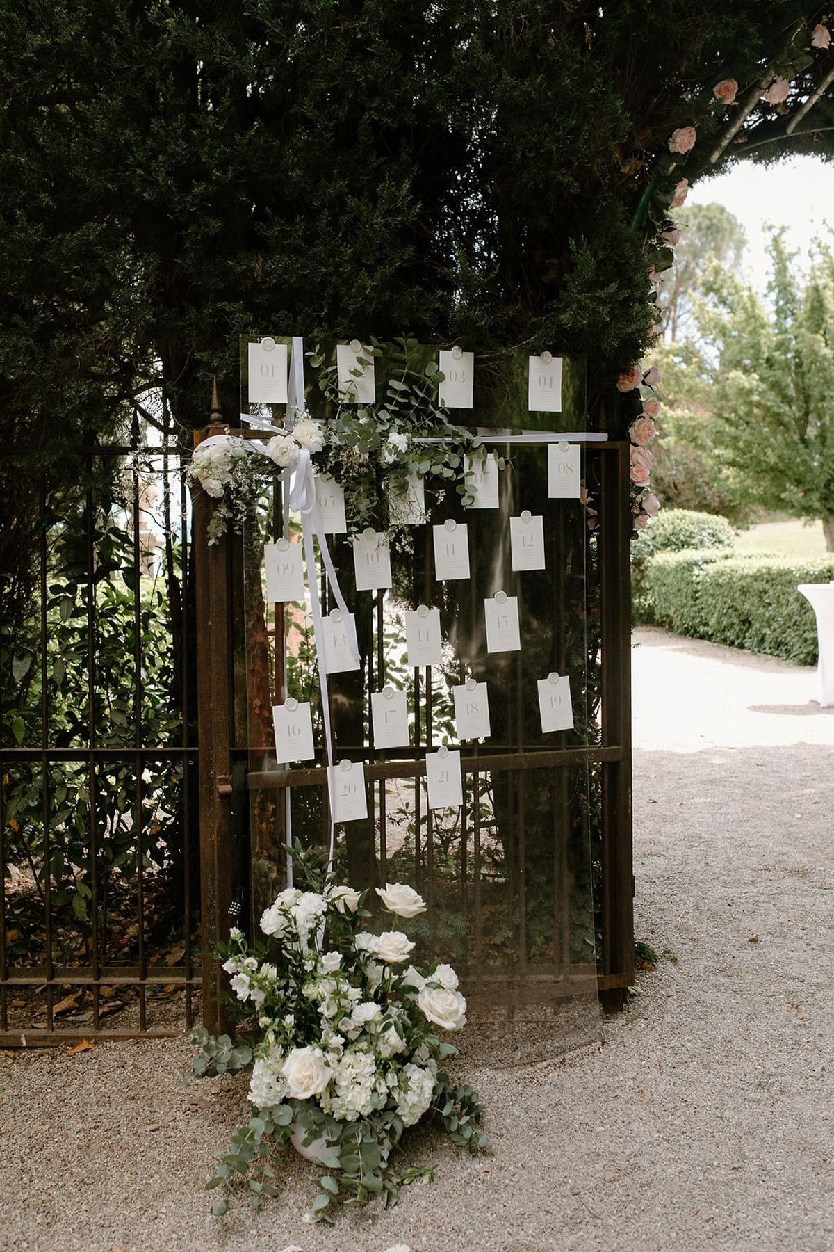 Seating chart cards pinned to antique iron gate with white rose and eucalyptus arrangement at Château Sainte-Roseline