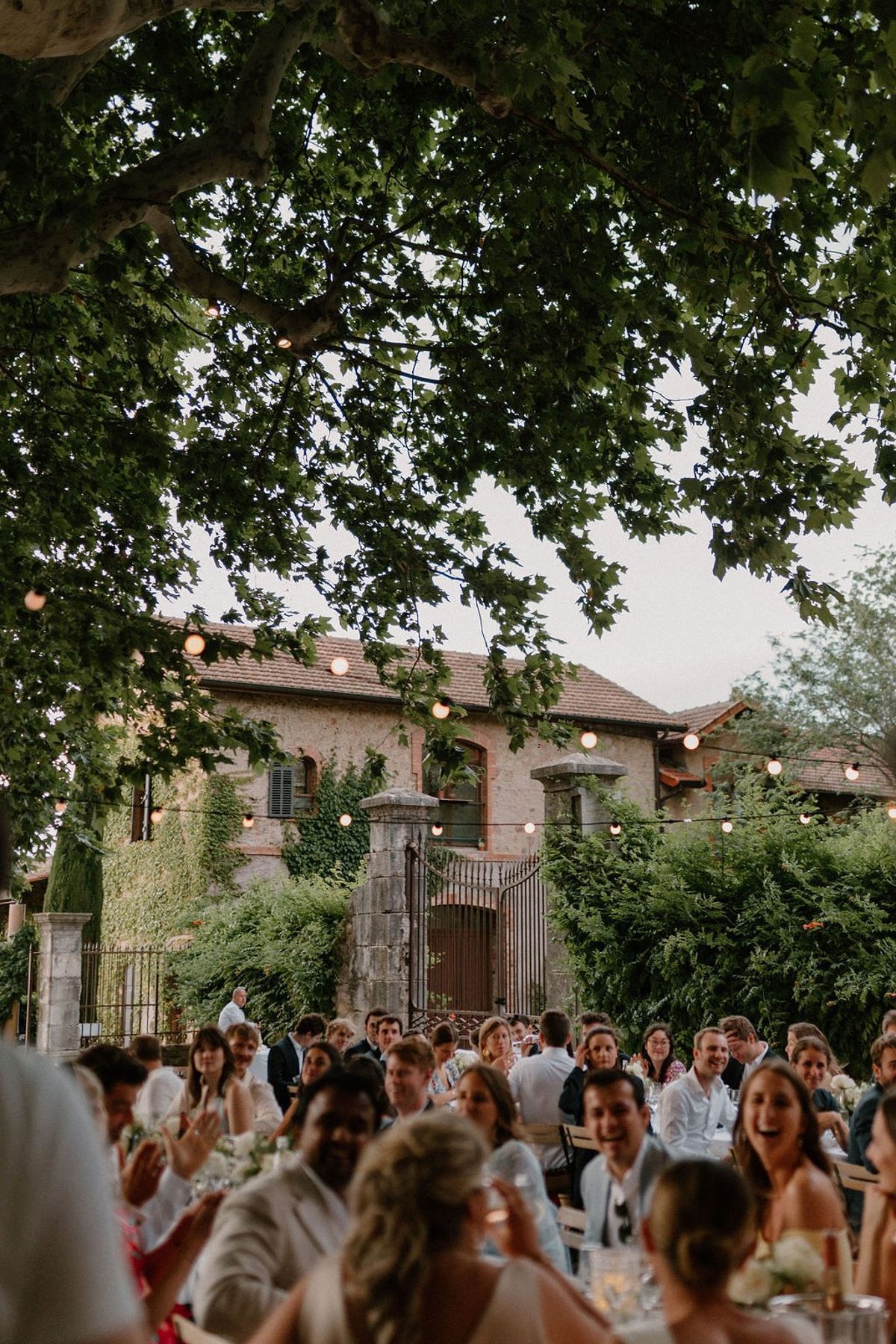 Guests seated at dinner under festoon lights with chateau facade and iron gate behind at Château Sainte-Roseline