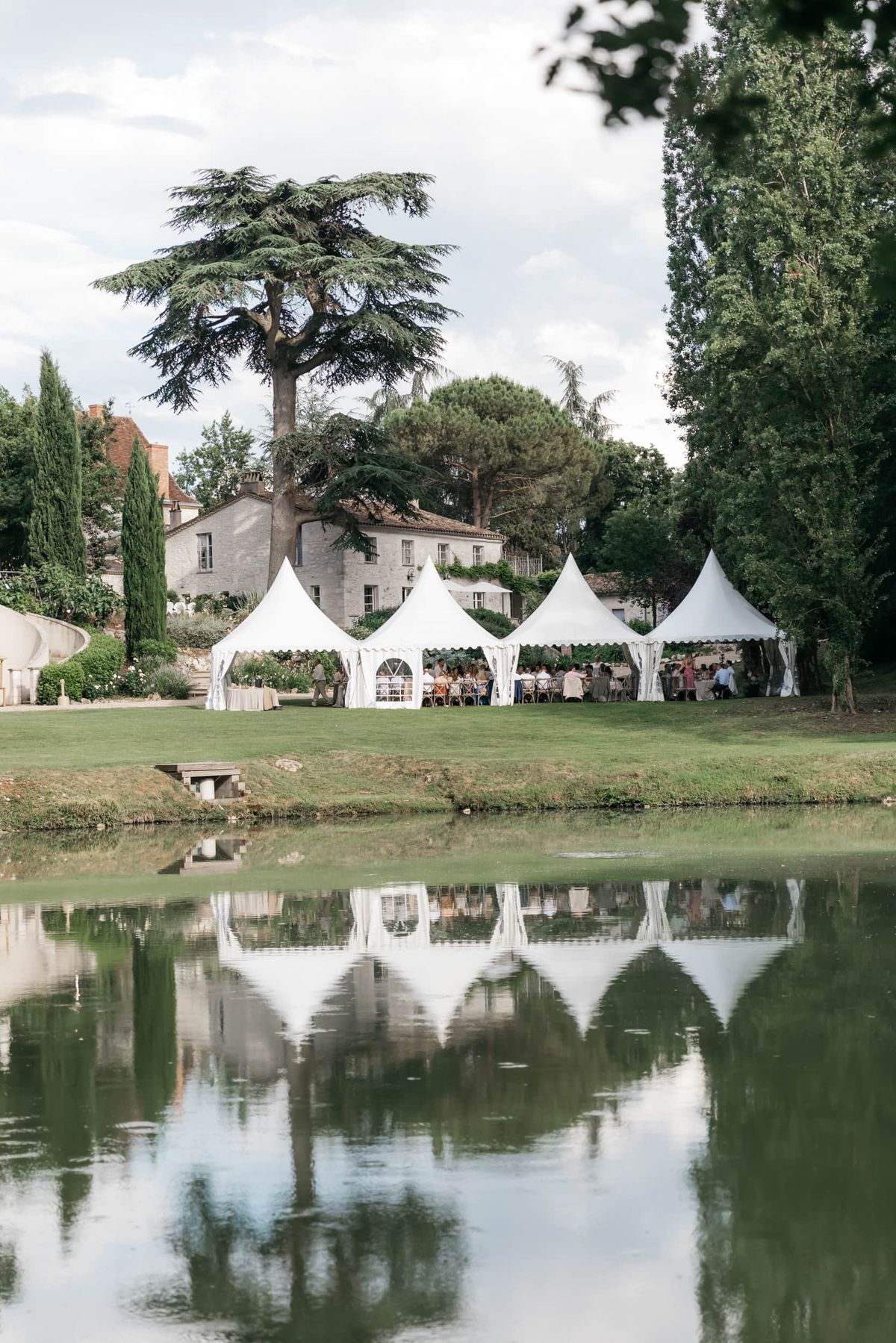 Four white pagoda marquee tents reflected in pond at French stone manor with 40 guests