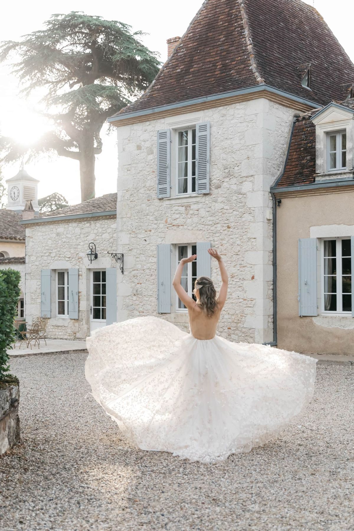 Bride twirling backless floral-applique ballgown in chateau courtyard with conical tower at golden hour
