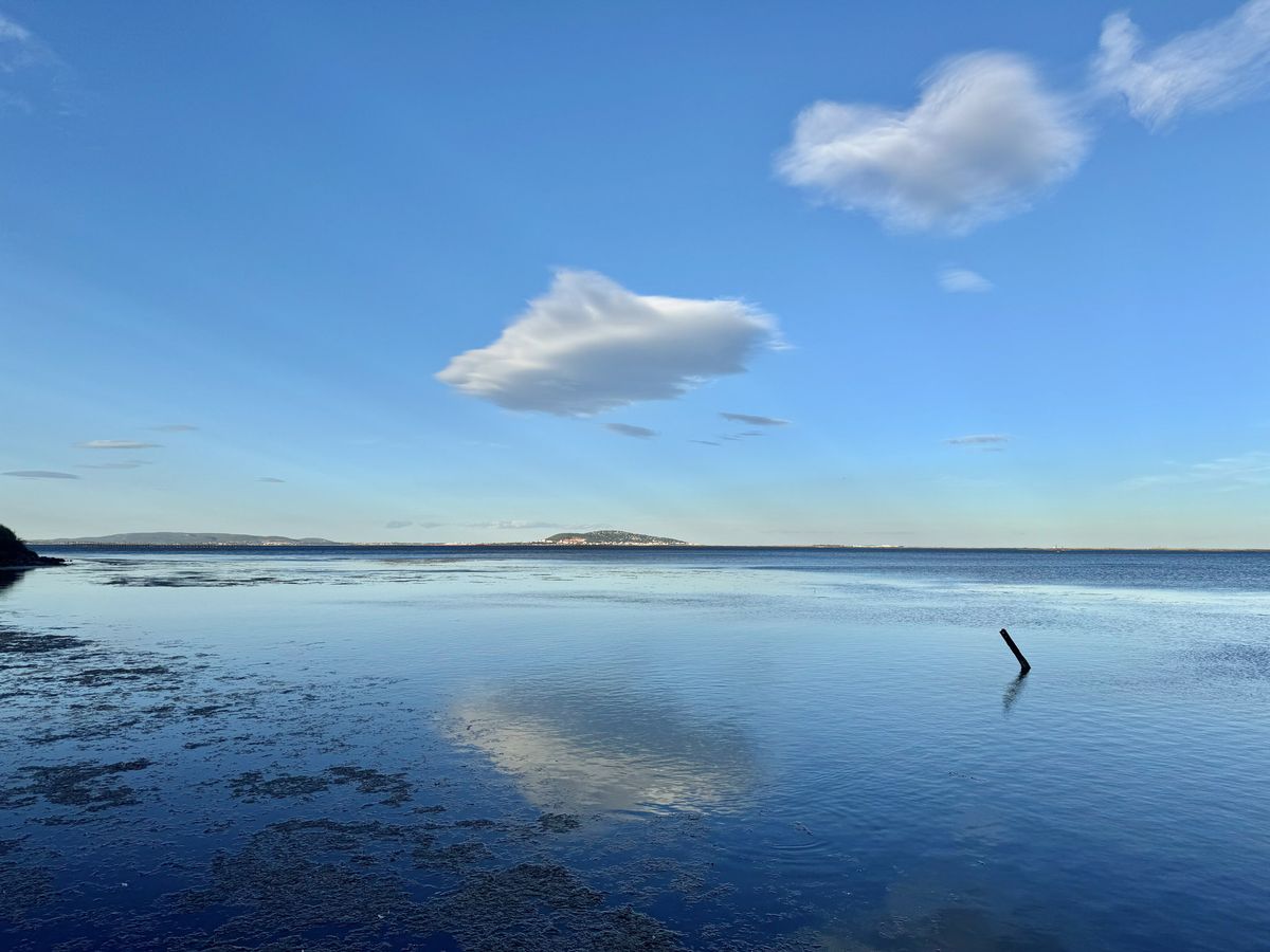 This image does not appear to be a wedding photograph. It shows a wide landscape shot of a calm body of water with no people, wedding-related subjects, decor, or event activity visible. A single wooden post protrudes from the water on the right side of the frame. This image does not belong in a wedding content library.
