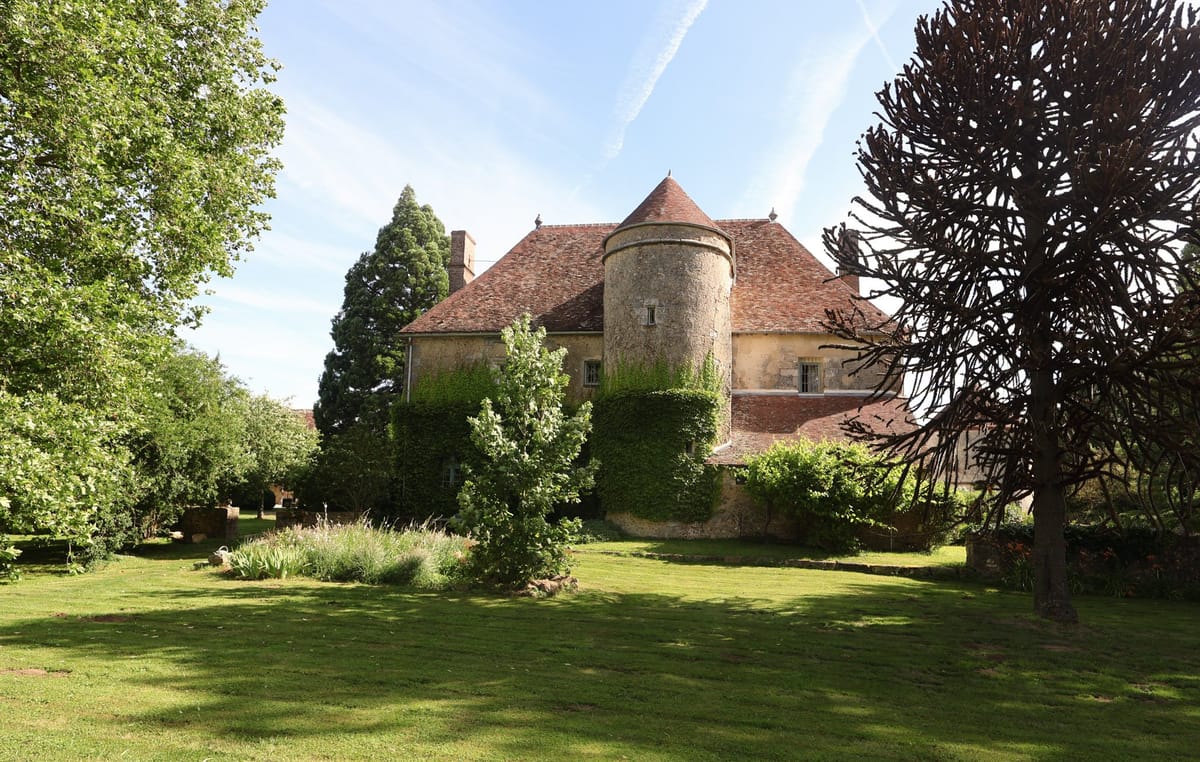 French chateau exterior with ivy-covered tower and terracotta roofs viewed from lawn with monkey puzzle tree