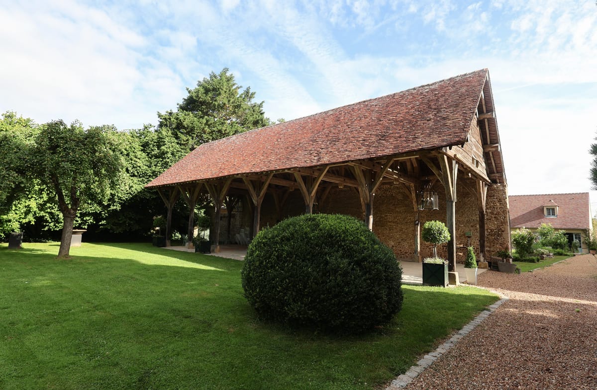 Oak timber-frame barn with terracotta roof, black planters, and spherical box hedge on gravel drive