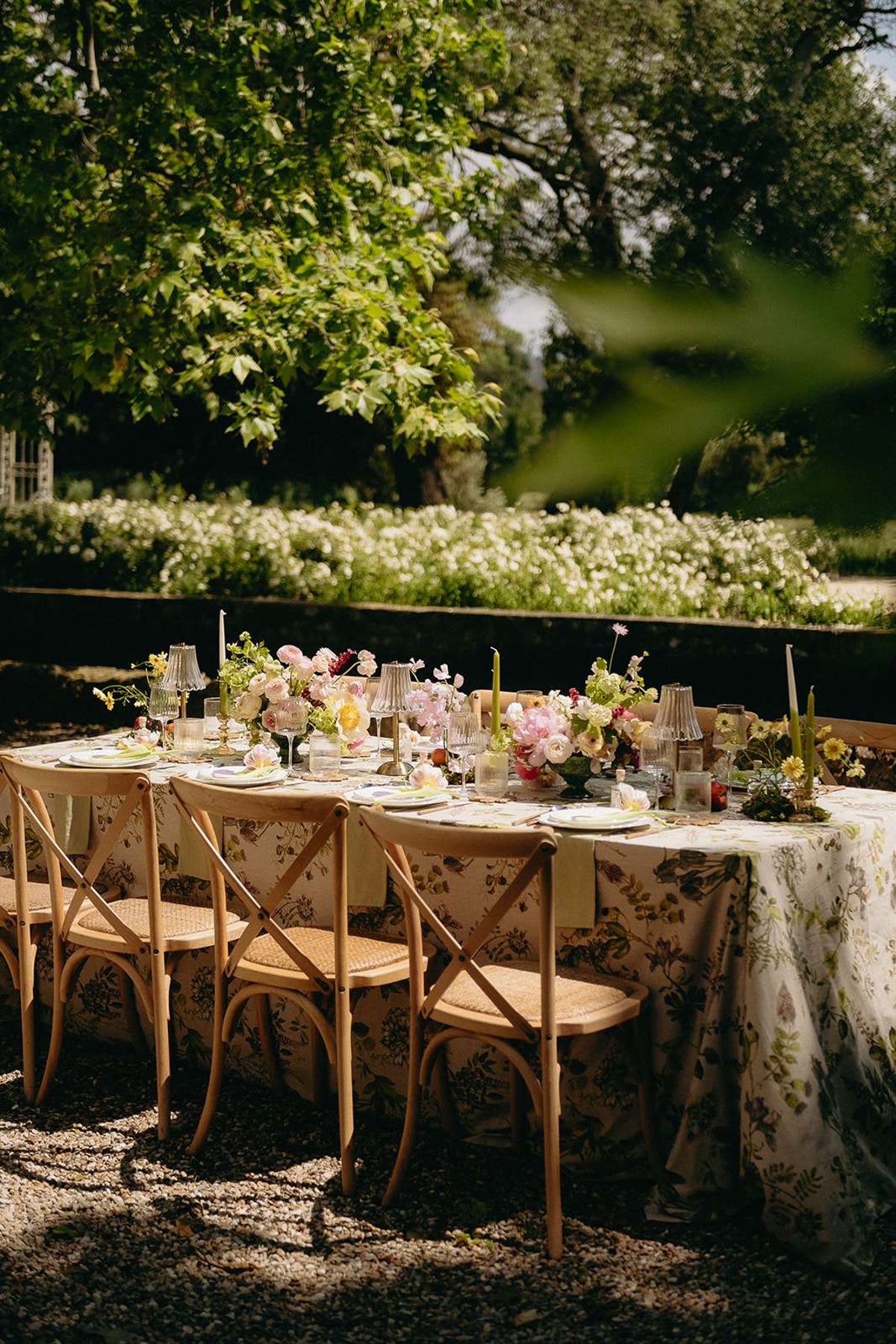 Garden reception table with botanical-print linen, pink ranunculus, yellow poppies, and olive taper candles