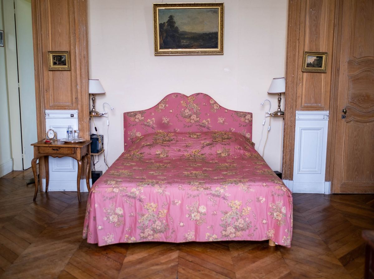Guest bedroom with rose-pink floral bedspread, oak paneling, and gold-framed oil paintings