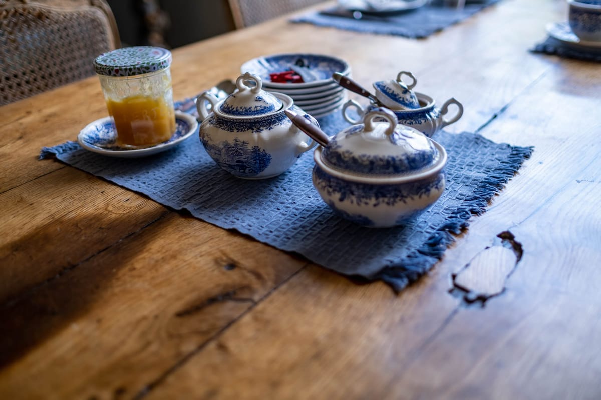 Rustic table with blue-and-white transferware china, honey jar, and fringed slate-blue linen placemats