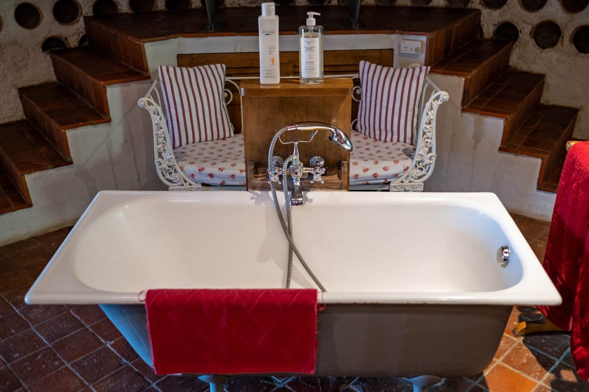 Venue bathroom with freestanding bathtub, wrought-iron chairs, and terracotta tile floor
