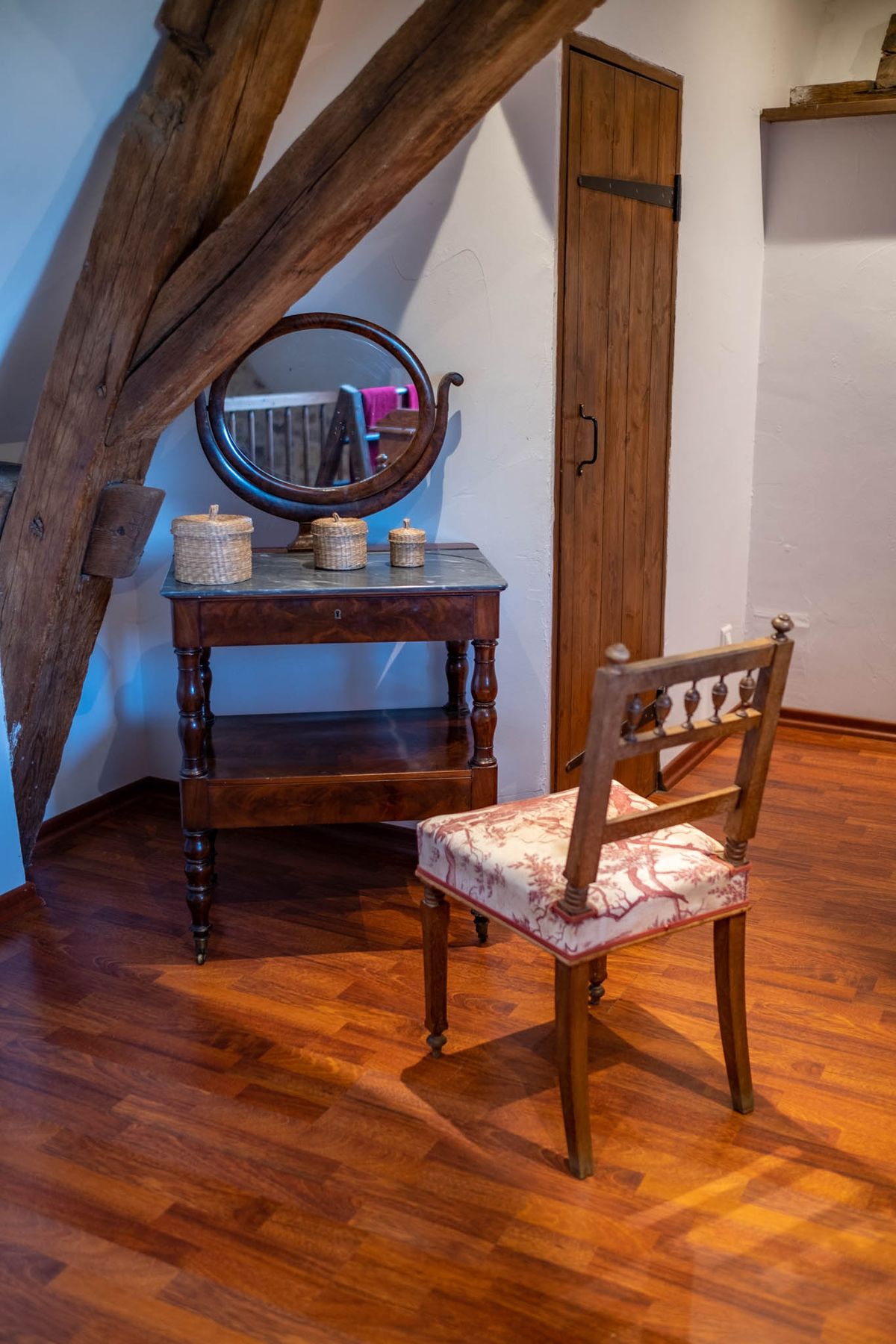 French chateau getting-ready room with exposed beams, antique vanity, oval mirror, and toile de Jouy upholstered chair