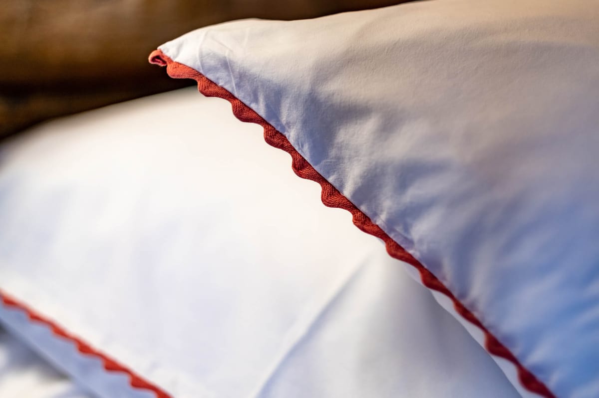 Close-up of white bed linens with terracotta red rickrack trim on pillowcase and sheet