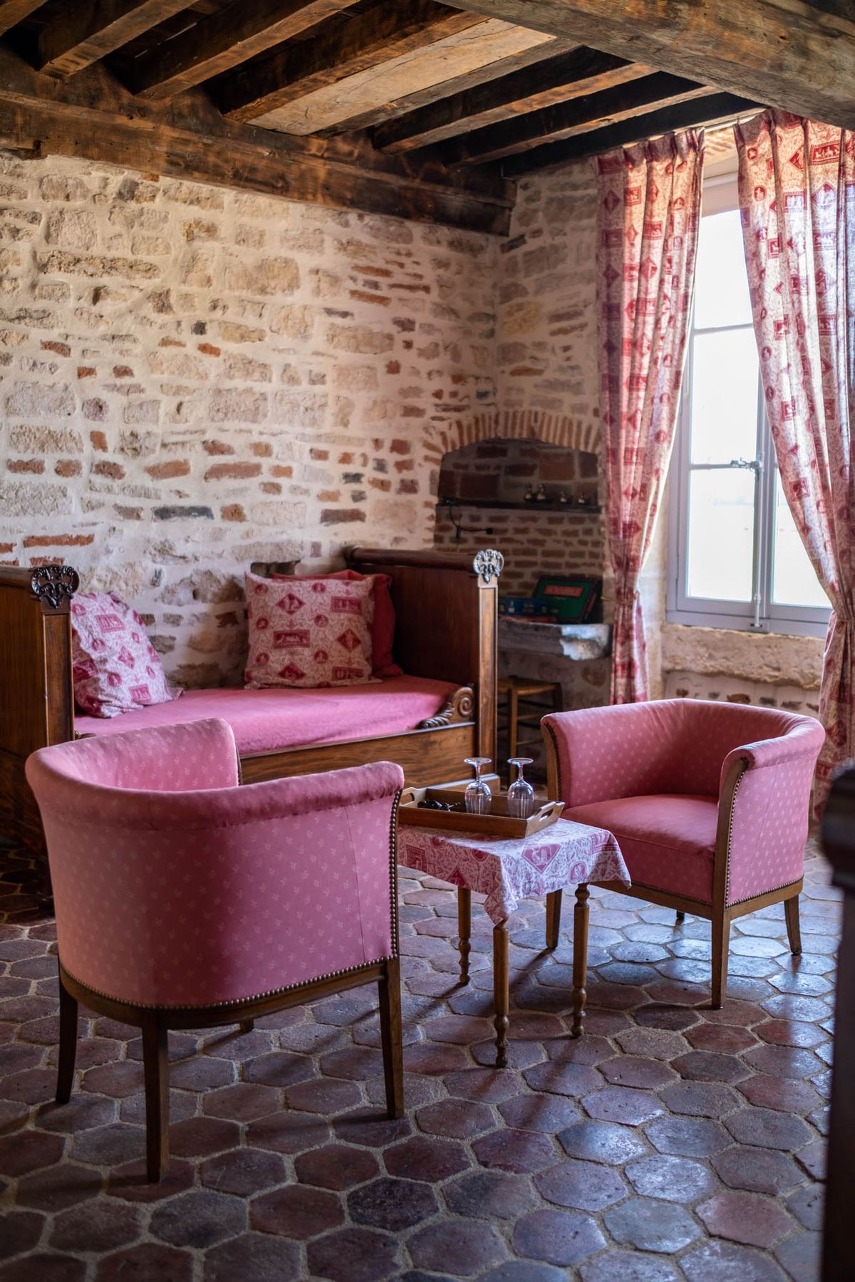 Rustic chateau room with stone walls exposed beams raspberry armchairs and toile de Jouy daybed