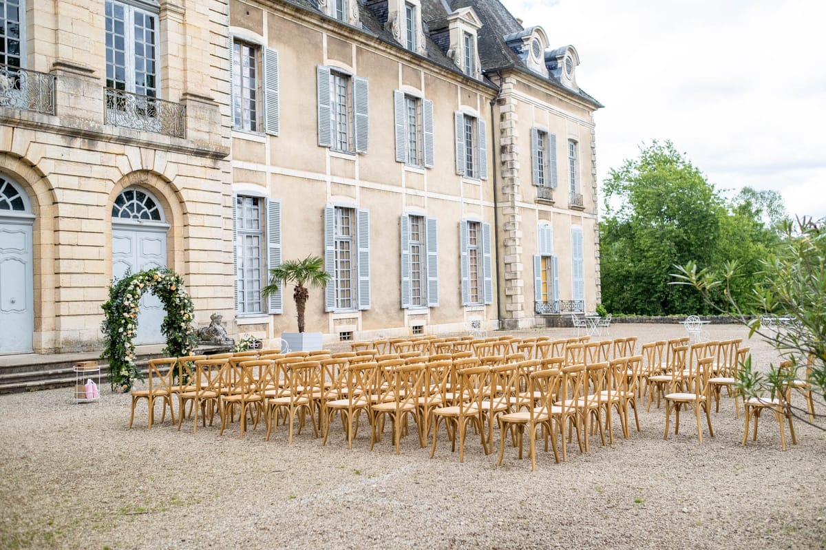 Crossback chairs facing peach and ivory floral arch at three-storey chateau with blue shutters