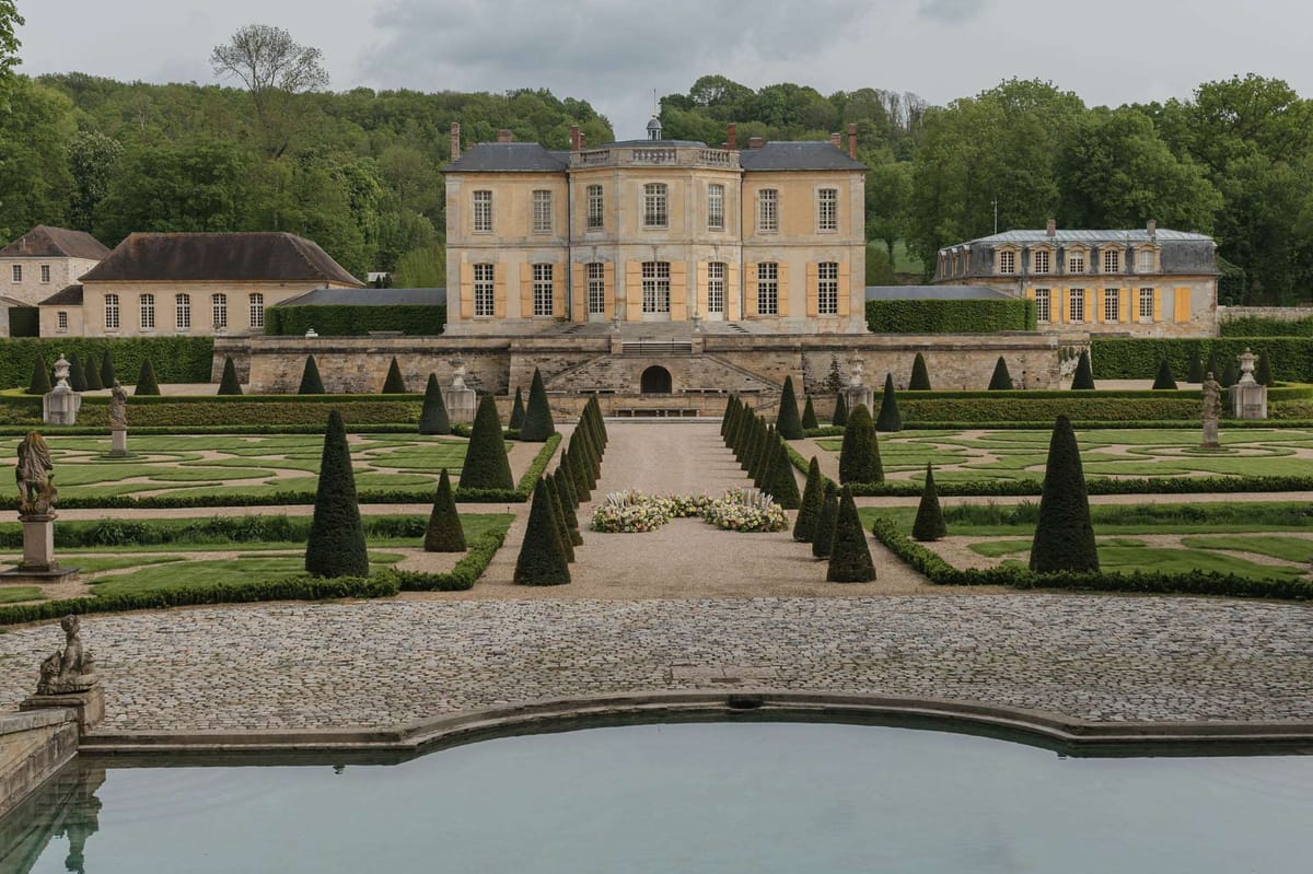 Classical chateau with conical topiaries, ornamental pool, and blush floral arrangement on central path