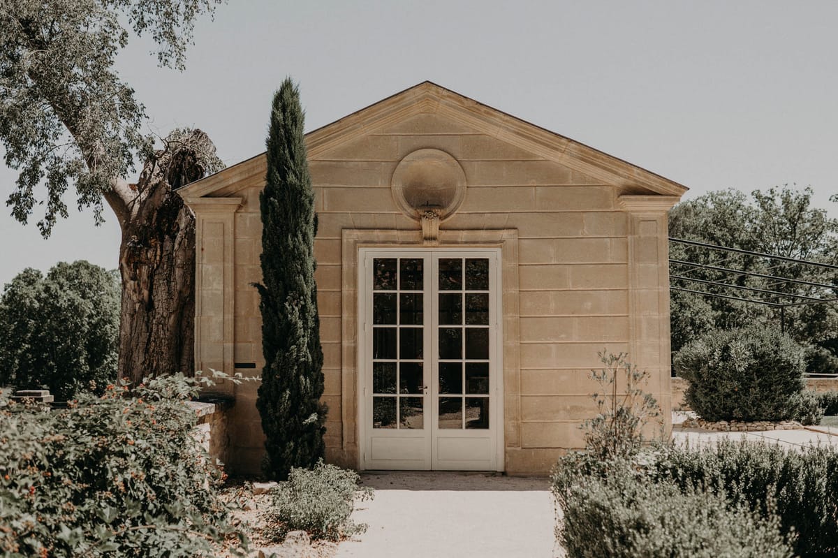 Classical limestone pavilion with triangular pediment cypress tree and gravel path bordered by ornamental shrubs