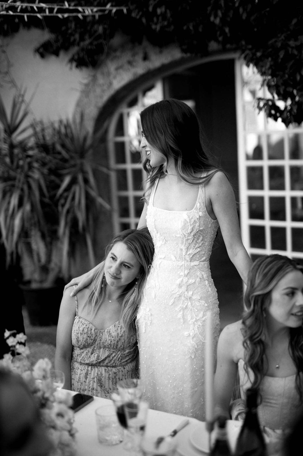 Black and white candid of bride sharing emotional moment with seated guest at reception table