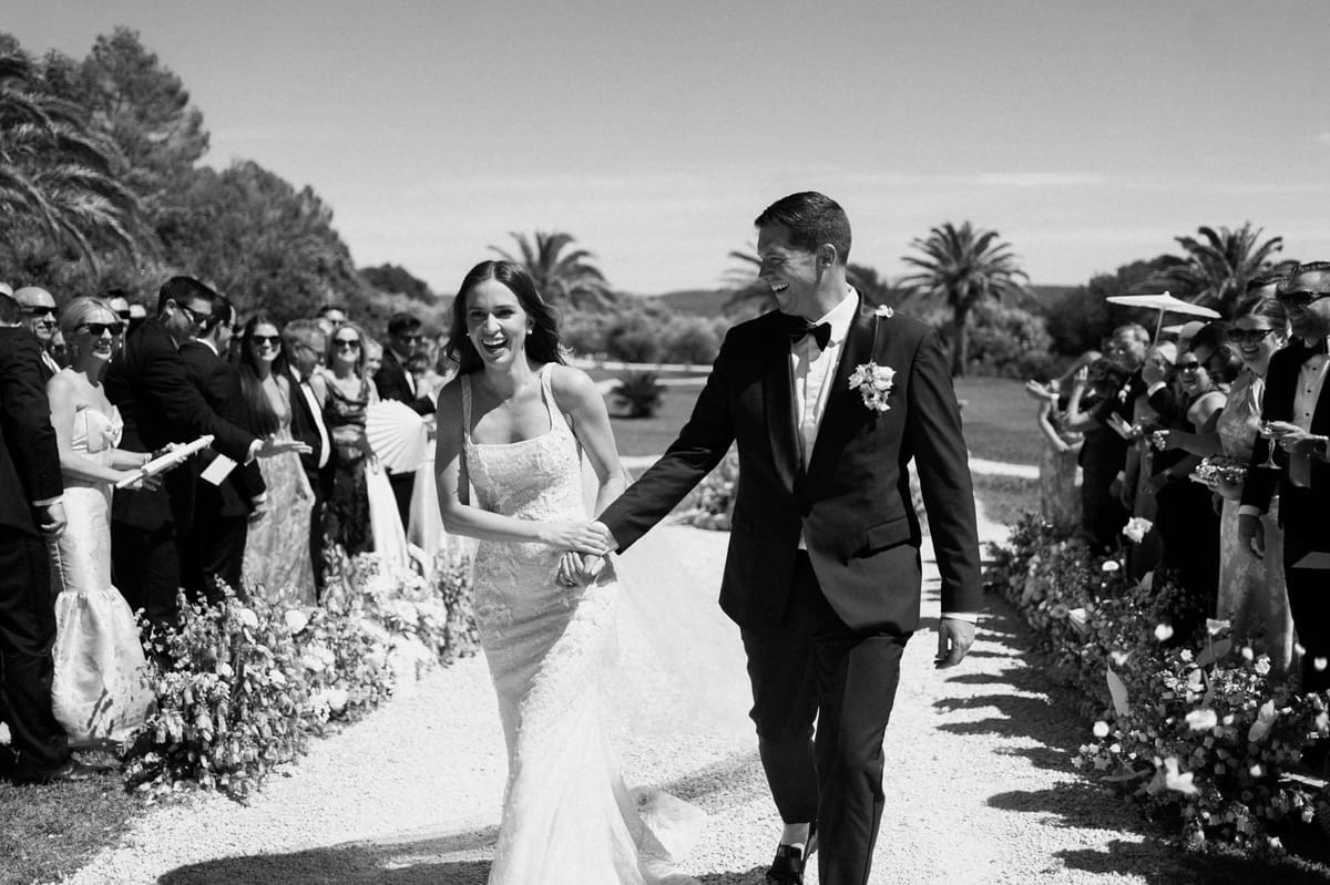 Black and white recessional with laughing bride and groom passing cheering guests with parasols