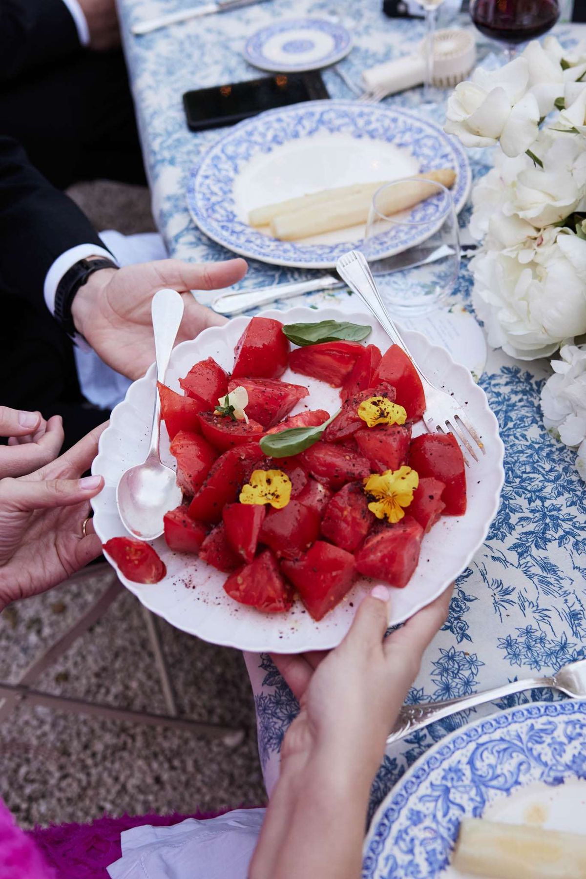 Hands serving tomato and watermelon salad on blue and white toile de Jouy tablecloth with patterned china