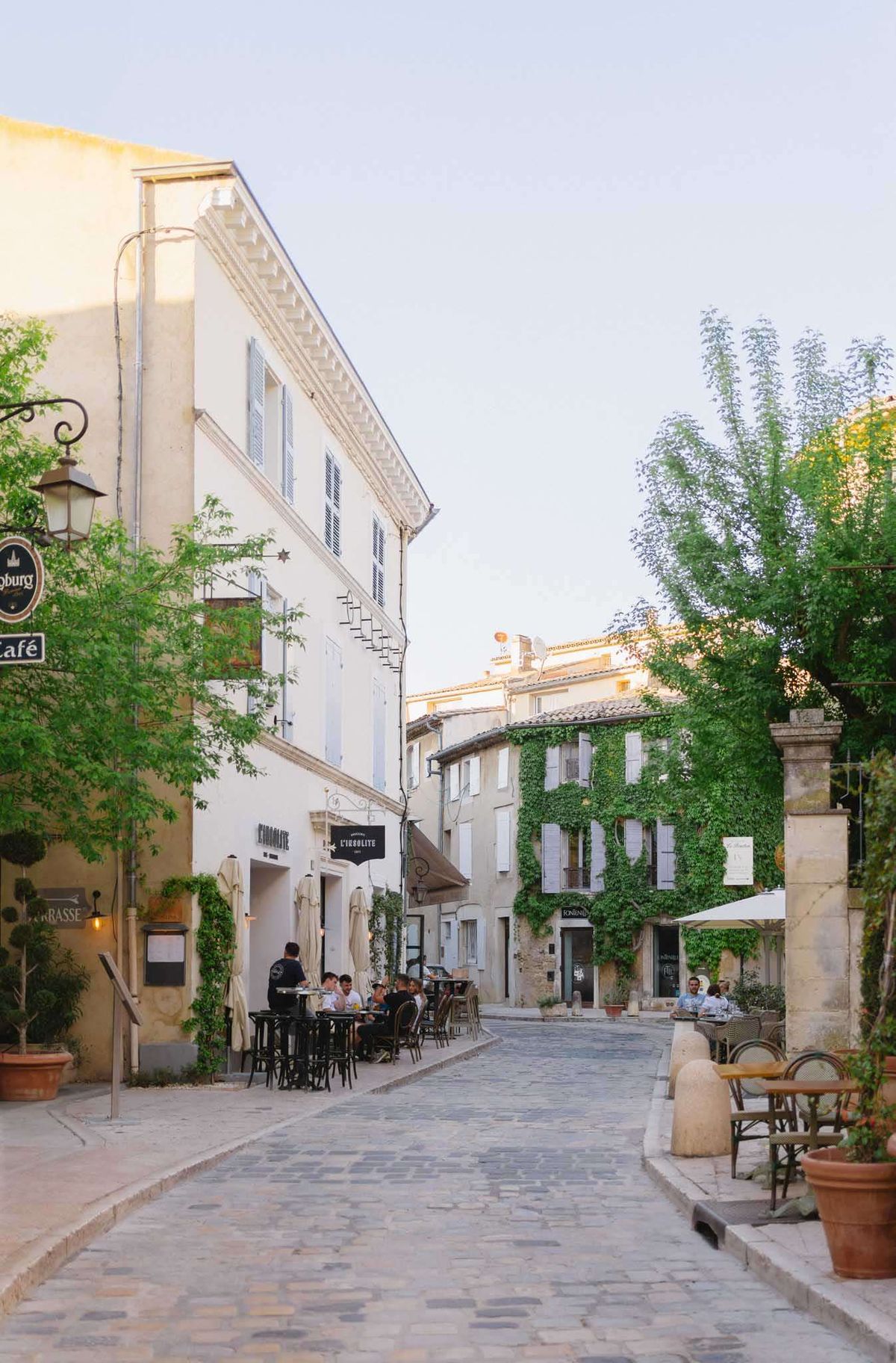 Provencal village cobblestone street with cafe terraces bistro chairs and stone buildings in warm afternoon light