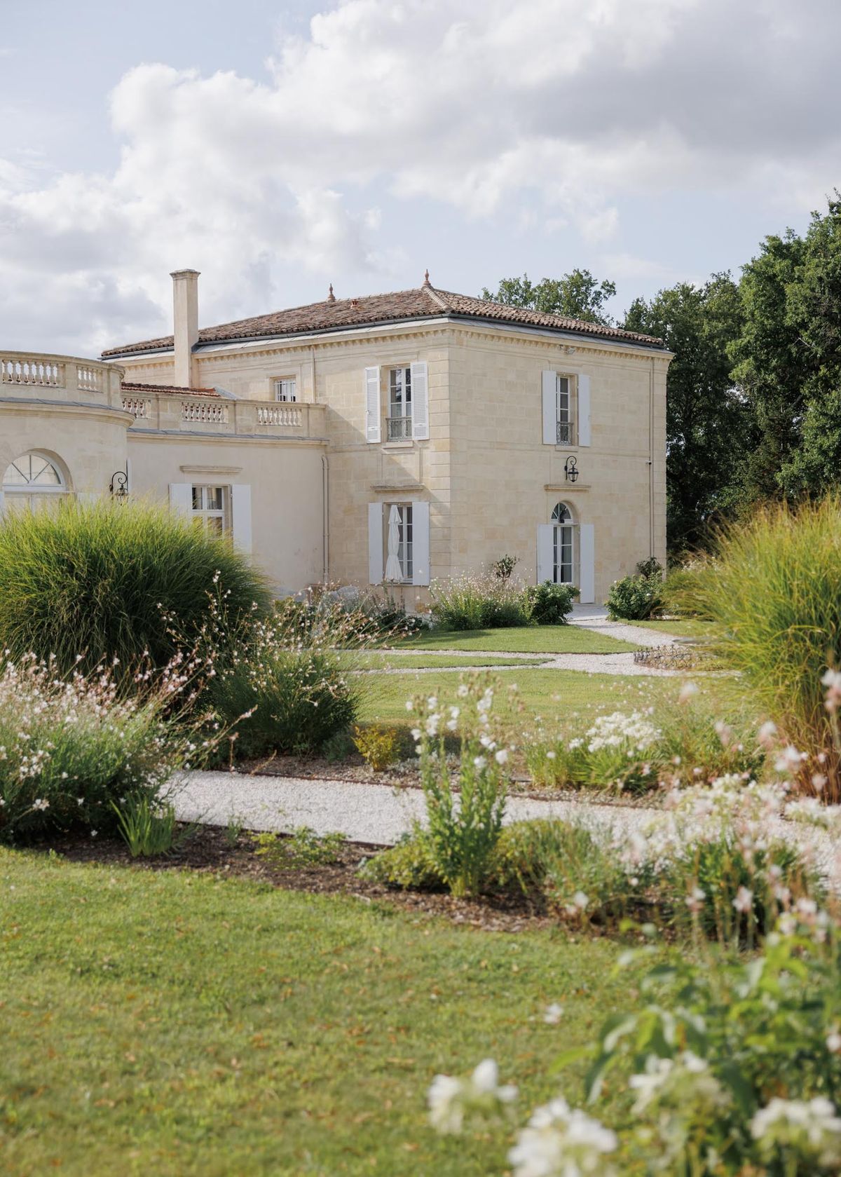 Cream limestone chateau with terracotta roof and landscaped garden beds from gravel approach path