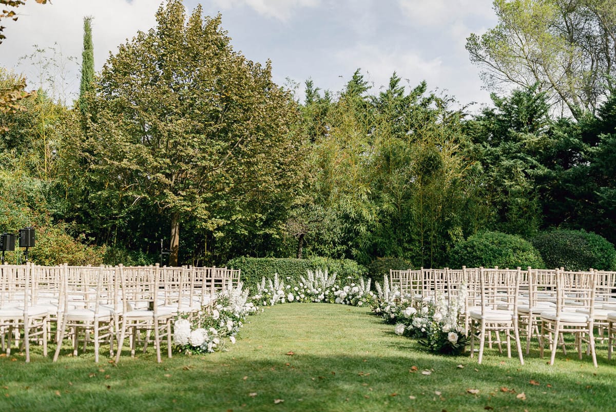 Outdoor ceremony setup with chiavari chairs on lawn and semi-circular white peony and hydrangea altar arrangement