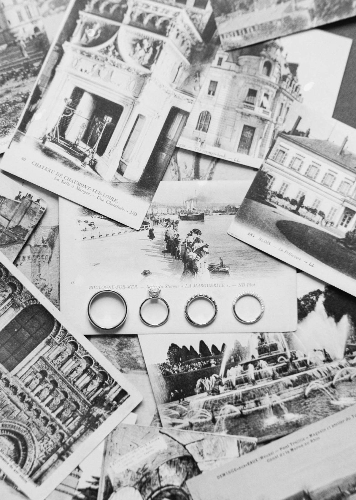 Black-and-white flat lay of four wedding rings arranged on vintage French postcards