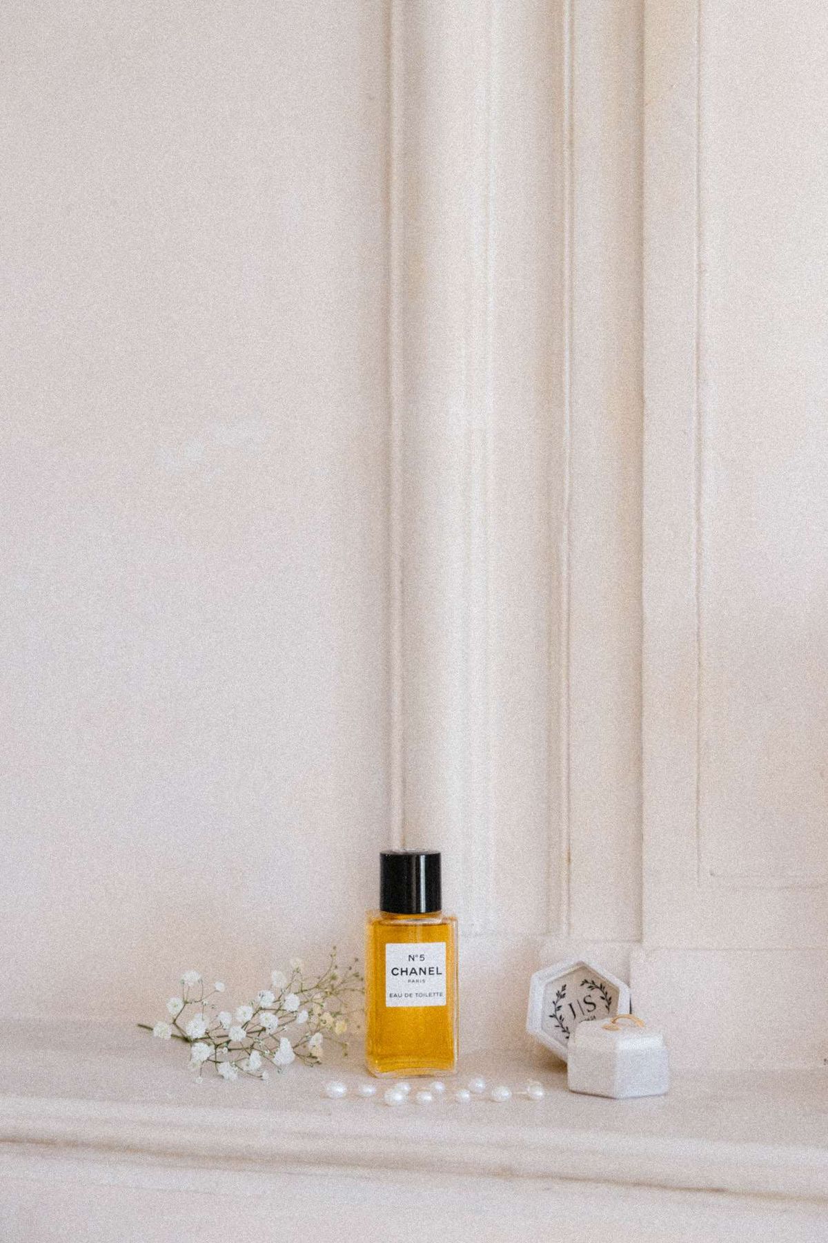 Getting-ready flat lay with Chanel No. 5, pearl beads, baby's breath, and gold wedding bands in velvet ring box