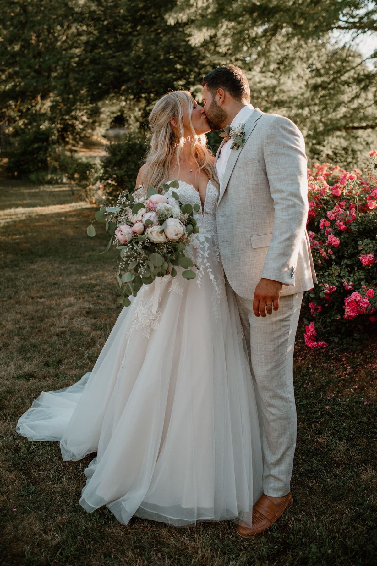 Couple kissing at golden hour, bride holding cascading blush peony and ivory rose bouquet with eucalyptus