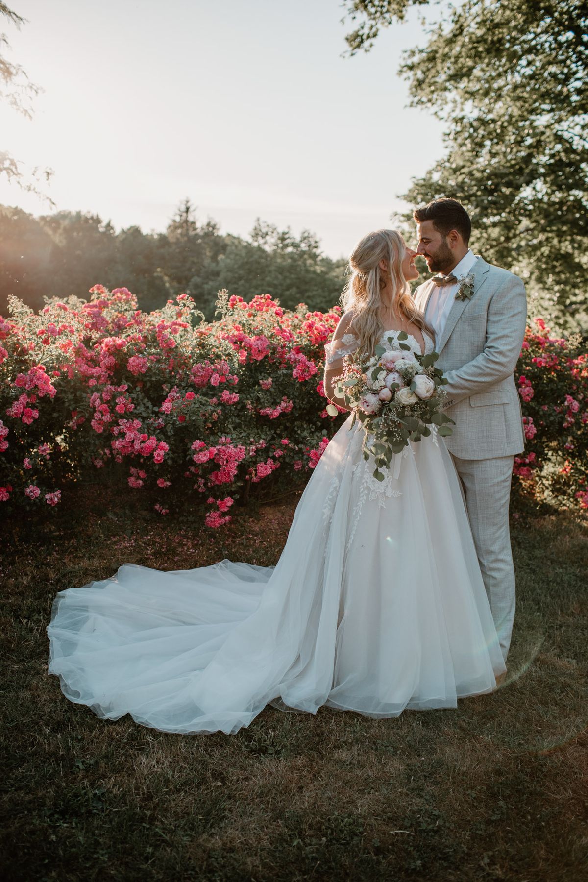 Bride and groom touching foreheads in a garden at golden hour with cathedral train spread across the lawn