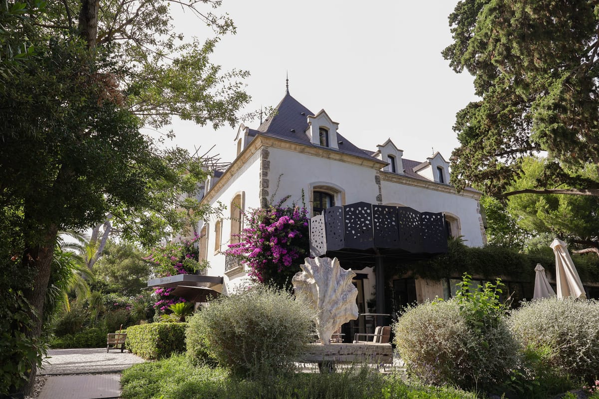 White rendered manor with slate mansard roof magenta bougainvillea sculptural shell and Mediterranean shrubs