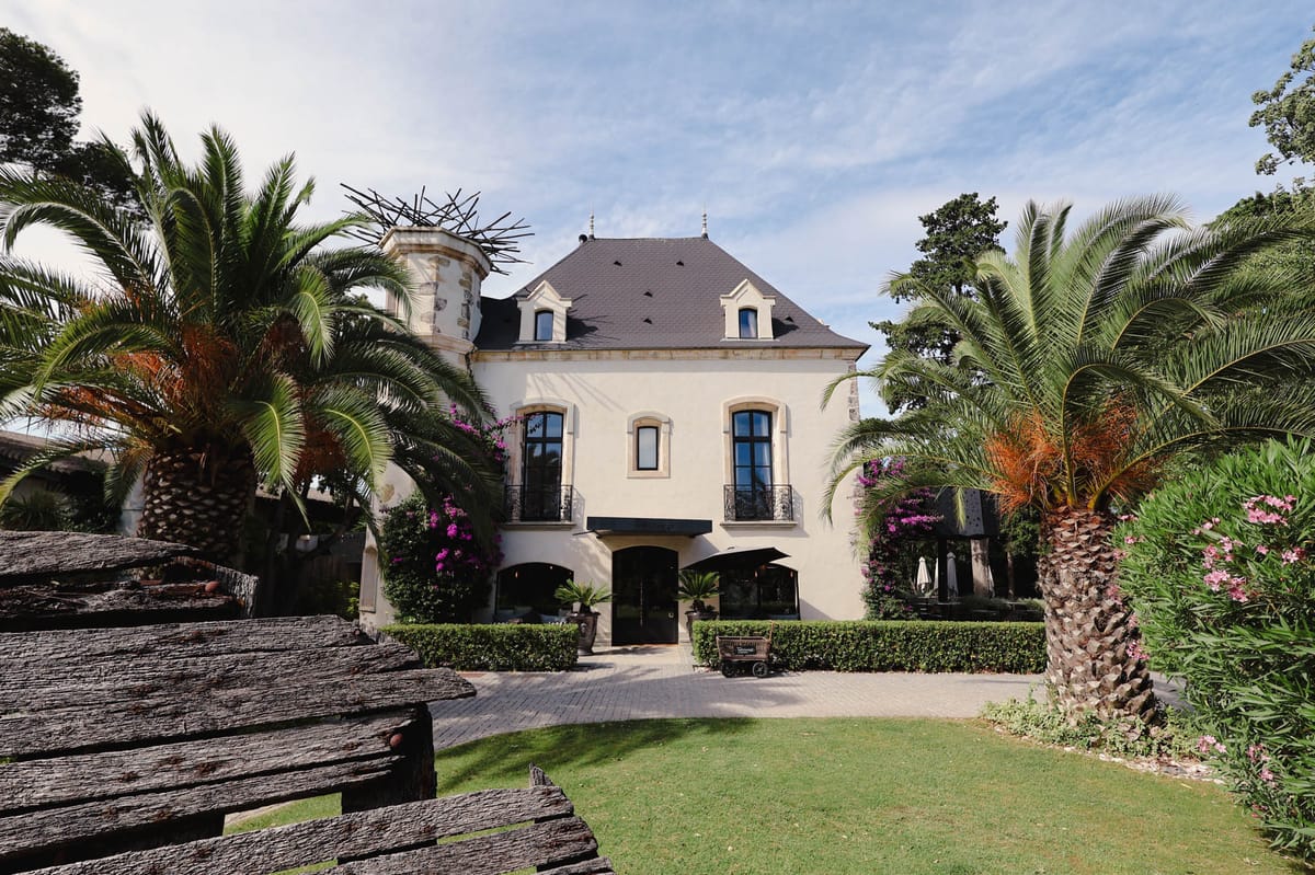 Cream manor with mansard roof, wrought-iron balconies, and magenta bougainvillea at entrance