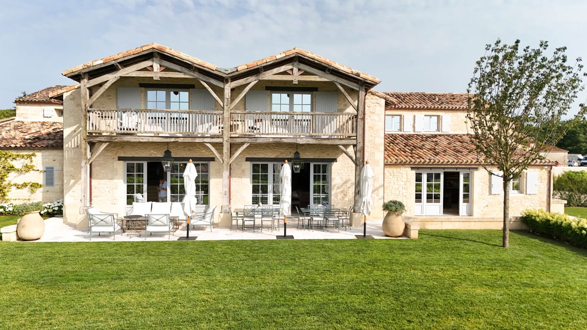 Cream limestone estate with timber gabling, full-width balcony, and white parasol terrace from lawn