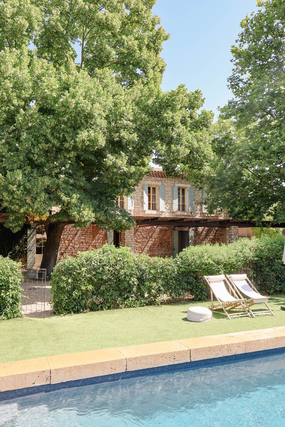 Provencal stone mas with terracotta roof wooden pergola pool deck chairs and clipped hedge from poolside