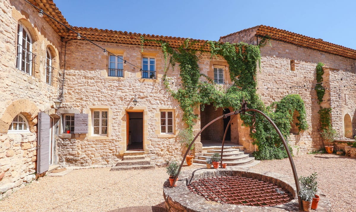 Golden limestone courtyard with stone well, iron arch, climbing vines, and string lights at historic priory