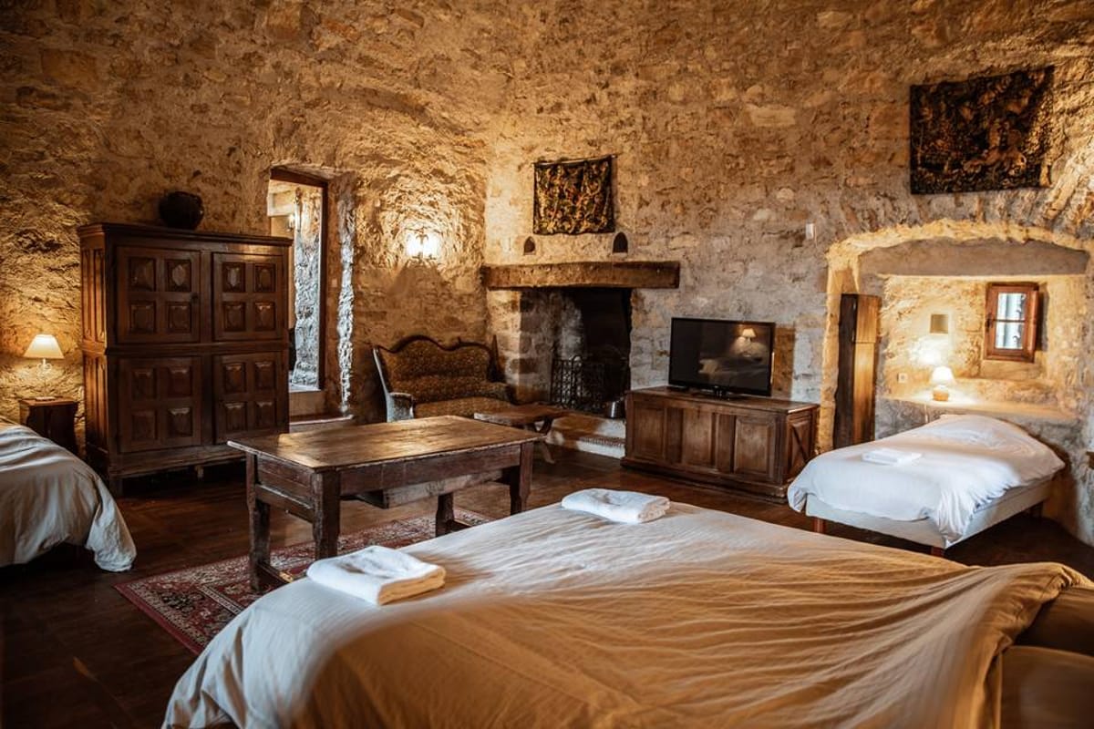 Stone-walled chateau guest room with vaulted ceiling, white-dressed beds, armoire, and fireplace
