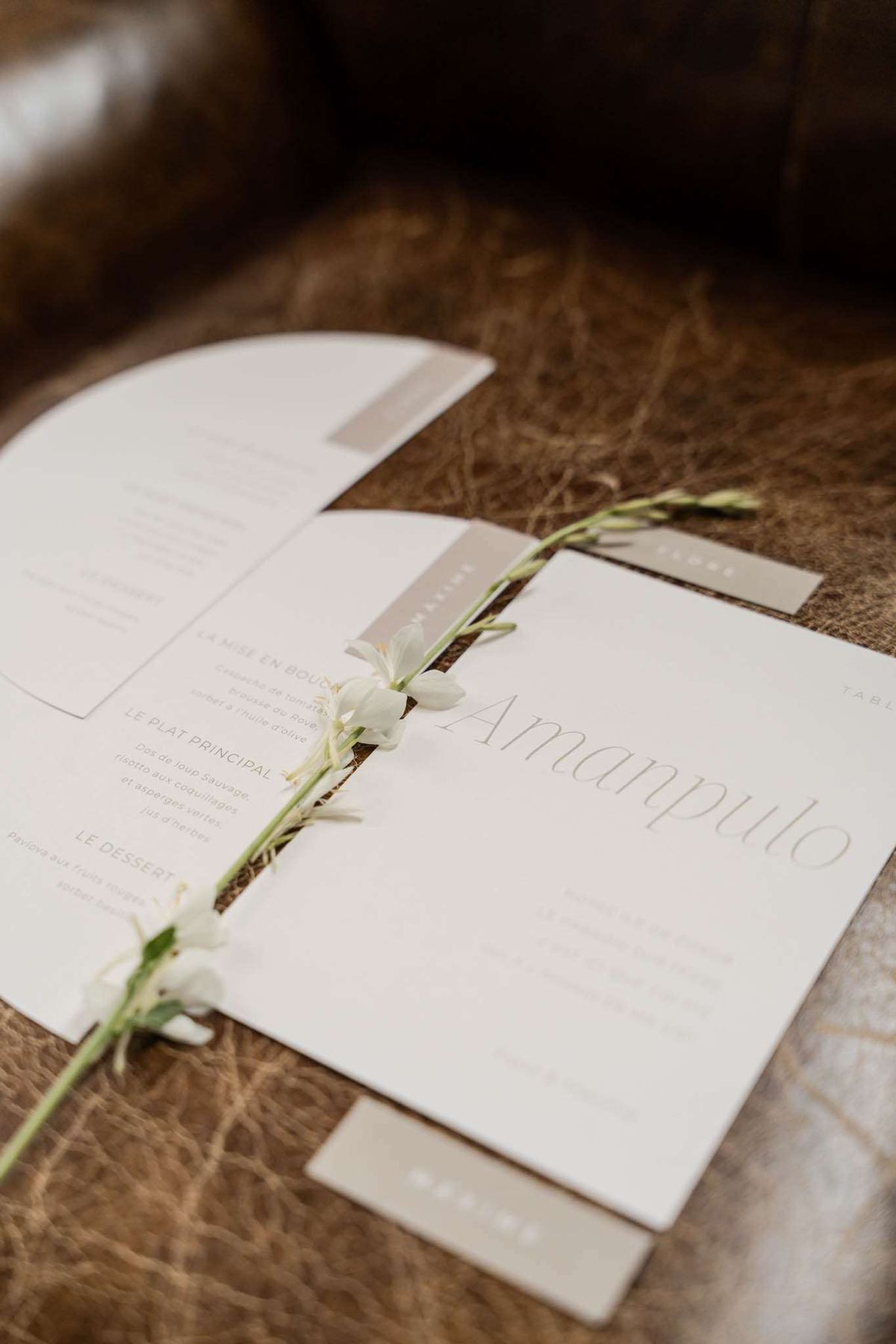 French menu card place card and table card with white freesia stem on textured brown surface