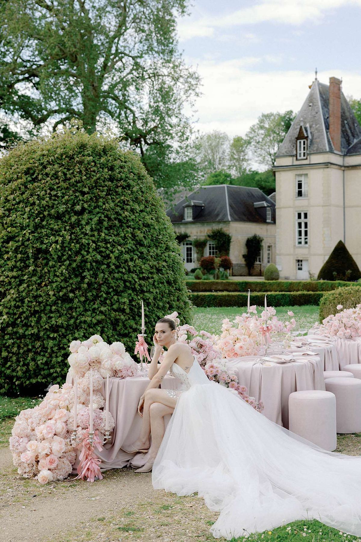 Bride at mauve linen table with cascading blush roses silver candelabras and ottoman seating before chateau