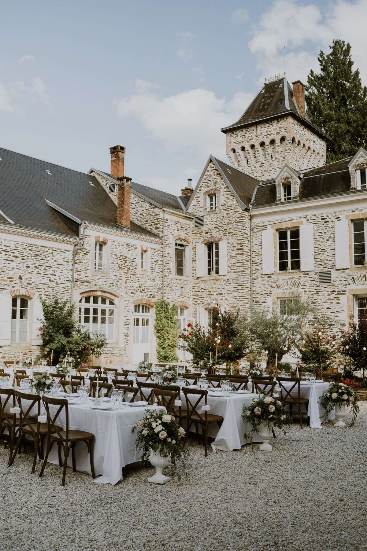 Chateau courtyard reception with cross-back chairs ivory and blush rose urns potted olive trees and candles