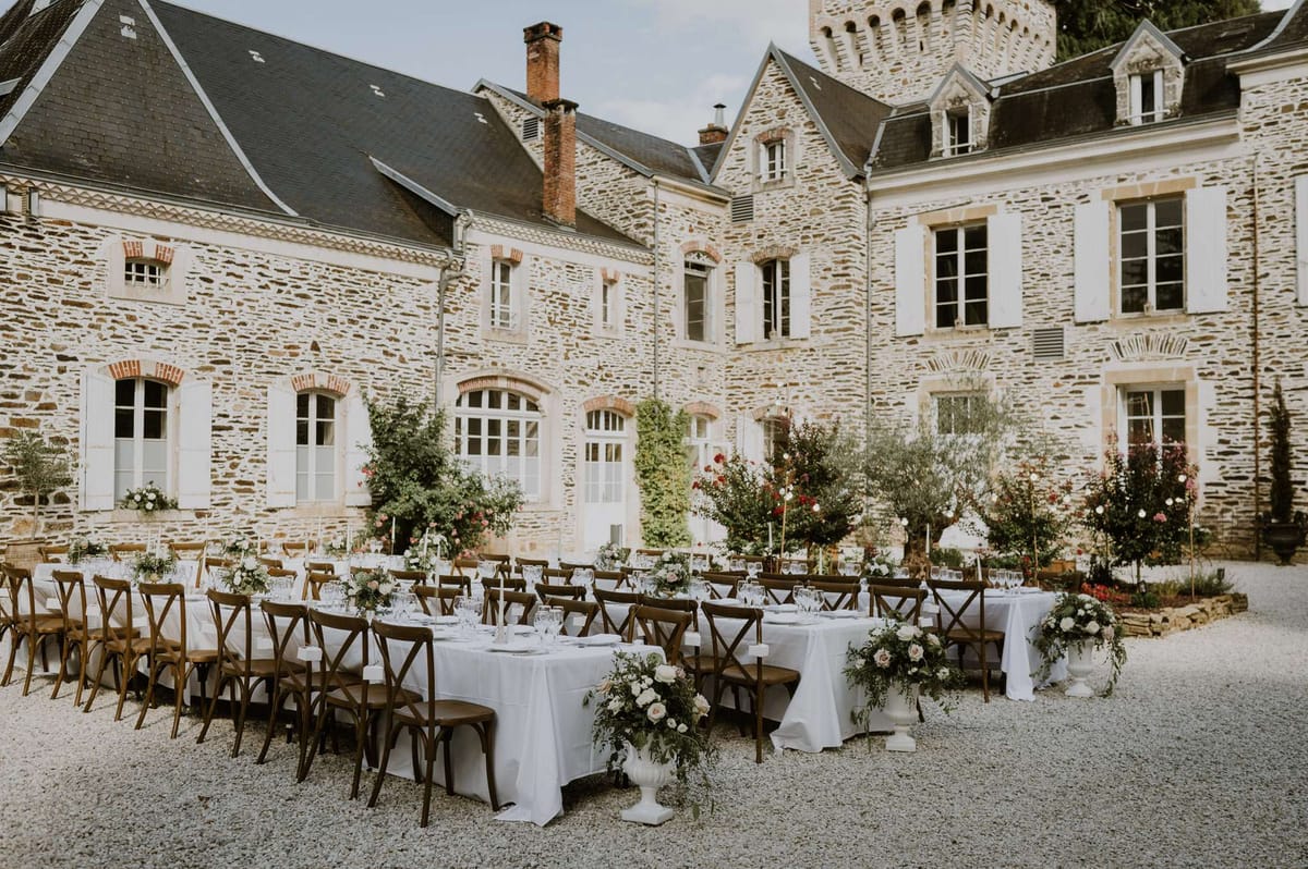 Three banquet tables with blush rose pedestals and gold candlesticks in chateau gravel courtyard