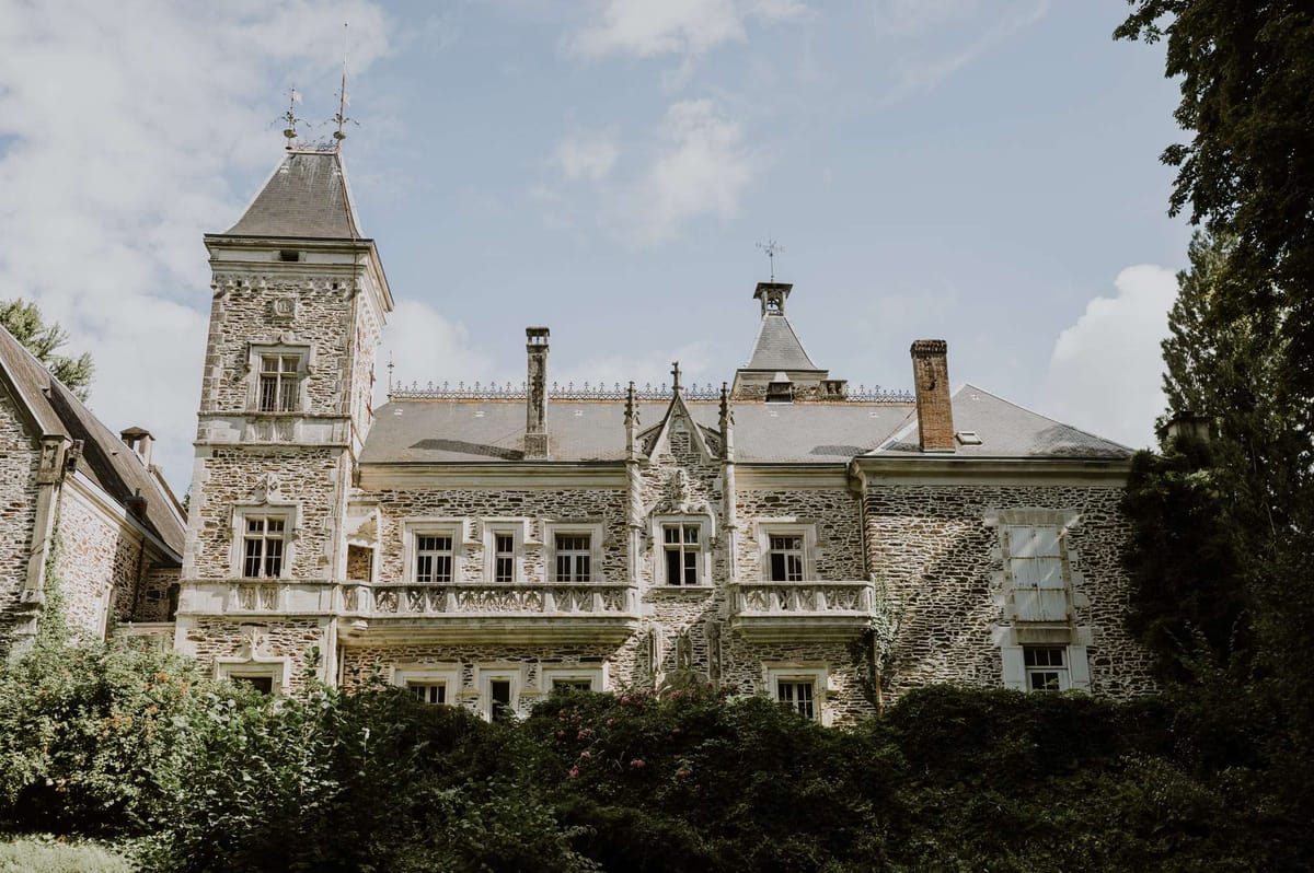 French chateau with corner tower, slate roof, white balustrades, ironwork cresting, and pink flowering plants