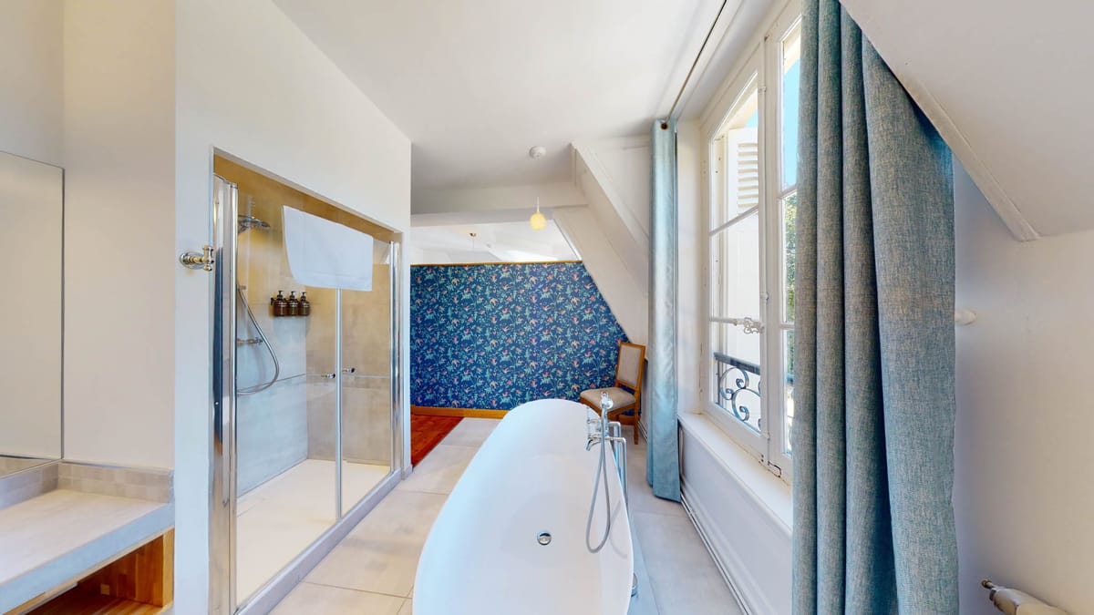 Attic bathroom with freestanding oval tub, navy botanical wallpaper, and glass shower in venue suite