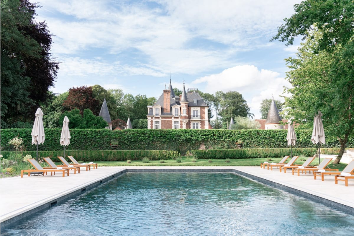 Red brick French chateau with slate turrets and rectangular pool with sun loungers on stone terrace