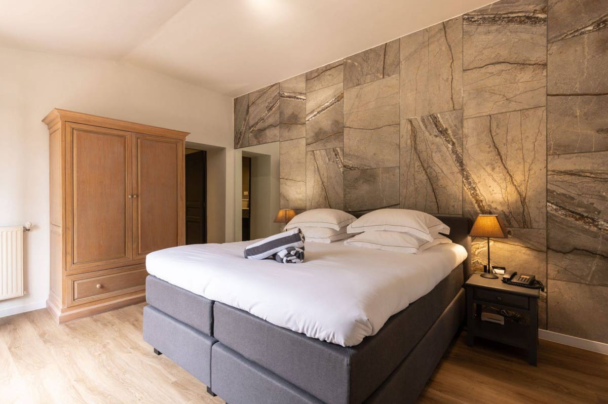 Contemporary guest bedroom with charcoal upholstered bed, marble-effect accent wall, and honey armoire