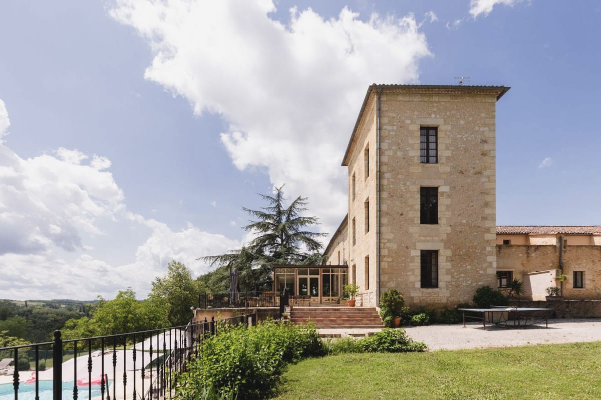 Golden limestone chateau with square tower, glass orangery, and gravel courtyard above rolling landscape