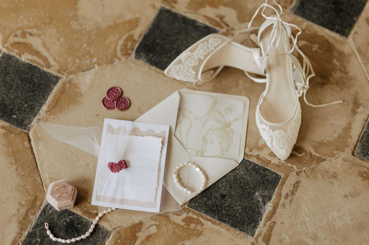 Bella Belle lace heels, wax-sealed invitation, pearl bracelets, and ring box on terracotta tile floor