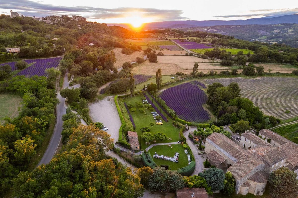 Aerial sunset view of U-shaped banquet table at a Provencal mas with lavender fields and hilltop village beyond