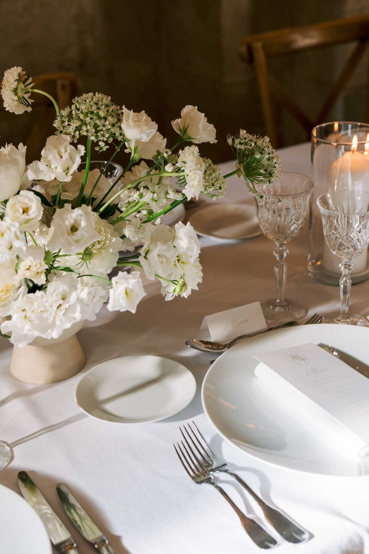 White lisianthus centerpiece in cream pedestal vase with porcelain plates and hurricane candle on linen table