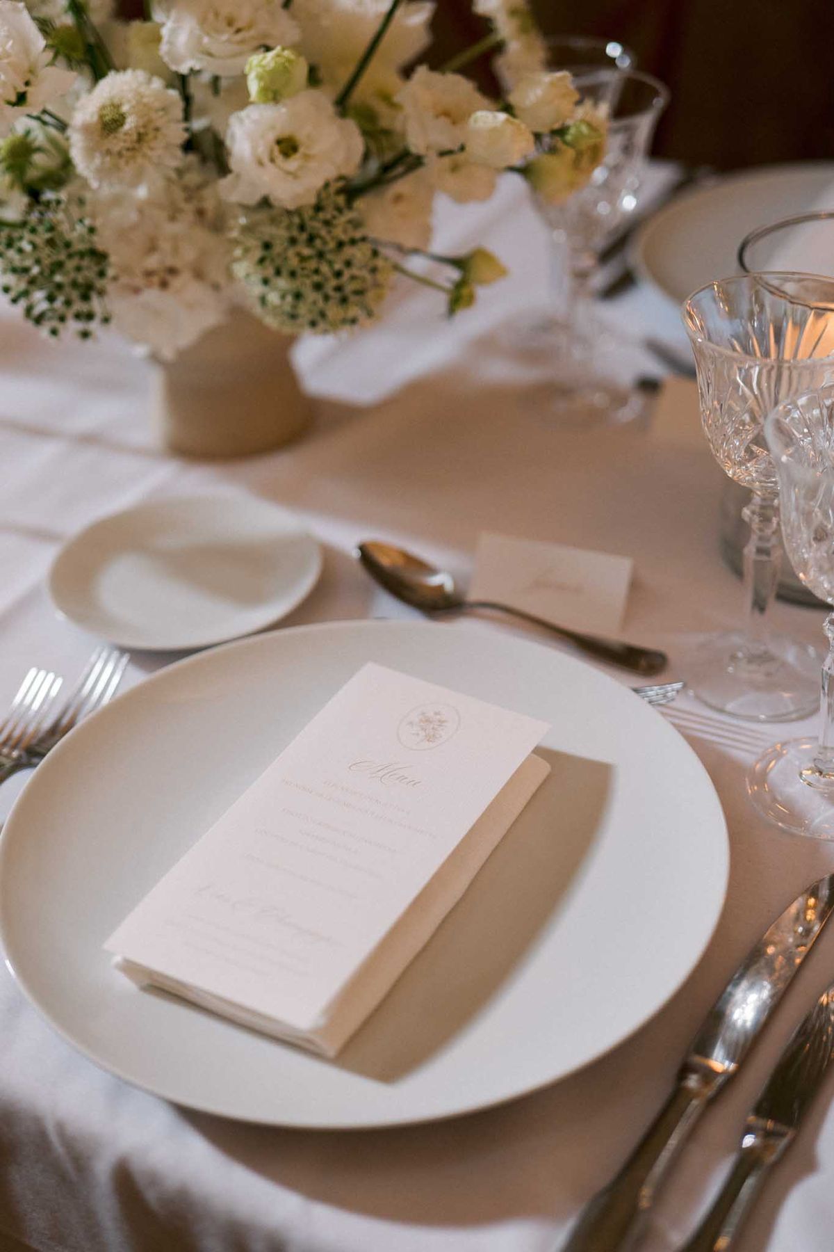 Reception place setting with printed menu card, kraft napkin, crystal glasses, and ivory lisianthus centerpiece